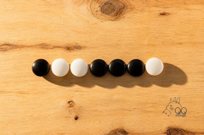 浅色松木桌面上七颗黑白围棋子一字排开,黑白随机交错